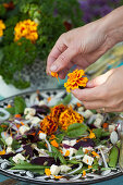 Hands plucking French marigold petals onto salad