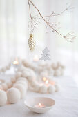 White wooden bead necklace and tealights on table and Christmas decorations hung from branch