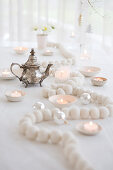 White wooden bead necklace, tealights and silver teapot on Christmas table