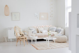 Couch with scatter cushions, tables, pouffe and chair with sheepskin rug in festively decorated white living room