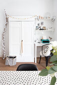 Festively decorated white cupboard between desk and chair and branch decorated with cotton ball fairy lights
