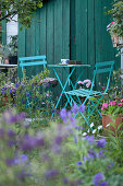 Turquoise garden furniture against petrol-blue board wall in flowering garden
