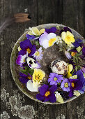 Wreath of flowers made of primroses, pansies, and anemones on a rustic plate