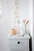 Wooden cupboard with flower and bowl, above a message and paper garland