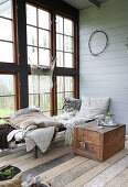 A wooden chest next to a day bed with blankets in a glass house