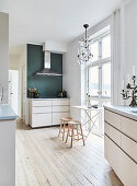 A filigree table and stools in front of a window and a kitchenette with an extractor fan