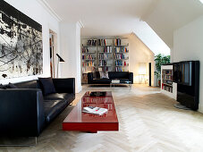 Black leather couch and red coffee table in the open living room, bookshelf in the background