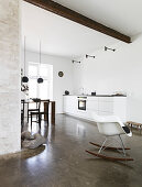 Rocking chair in an open living room with kitchenette and concrete floor