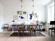 Black dining table with Thonet chairs in front of half-height bookcase and lithographs on white wall