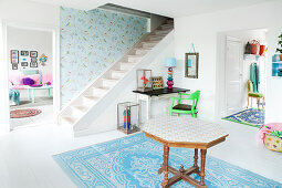 An octagonal wooden table on a blue-and-white rug in an anteroom with a white wooden floor and a staircase in background