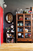 An antique china cabinet with glass doors next to a wall mirror and wooden boxes as storage containers