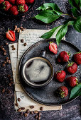 Tasse Kaffee auf Servierteller, daneben Erdbeeren