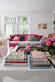 Blick über Couchtisch mit Büchern auf pink lackiertes Rattansofa mit bunten Kissen