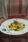 Frau serviert Artischockenravioli mit karamellisierten Zwiebeln und Oliven