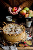 High autumn apple pie, in the background a person in a sweater holds an apple