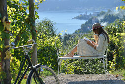 Woman reading book sitting on bench with sea view