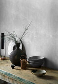 Keramikschalen und Vase auf rustikalem Tisch vor grauer Wand