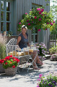 Terrasse mit Stammrose 'Heidi Klum', Geranien und Reitgras, Frau auf Bank genießt den Sommer
