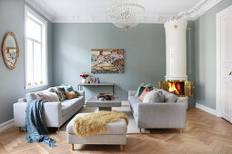 Sofa set, coffee table and Swedish tiled stove in living room with herringbone parquet floor