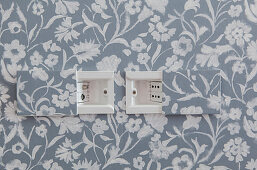 Plug sockets with sliding covers in wall with patterned wallpaper