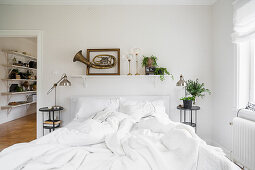 Old brass instrument in frame on wall above rumpled bed
