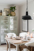 Fur rugs on wicker chairs around set table in dining room with glass-fronted cabinet