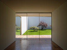 View from cubist, minimalist interior through glass wall onto wooden terrace and courtyard garden