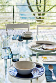 Place settings on glass dining table in front of glass window with garden view