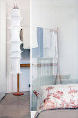 Bett mit Glastrennwand als Kopfteil, dahinter Ankleidebereich mit Designer-Stehleuchte und Herrendiener