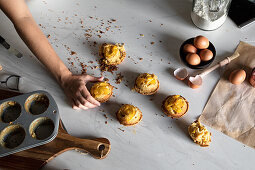 From above crop person hand holding a homemade cupcakes on wooden table with arranged eggs