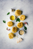 Nests of tagliatelle pasta with basil leaves and garlic on table