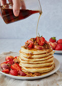 Ahornsirup fließt auf Pancakes mit Erdbeeren, Pfirsichen und Granola