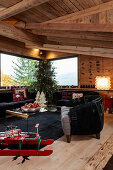 Roter Schlitten, schwarze Polstermöbel und geschmückter Weihnachtsbaum im Wohnzimmer eines Chalets