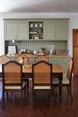 Wohnküche mit graugrünem Küchenschrank und Stühlen mit Flechtrückenlehnen an Esstisch