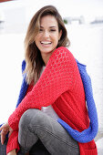 A young woman wearing a red knitted jumper with a blue jumper over her shoulders