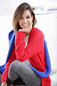 A young woman wearing a red knitted jumper with a blue jumper over her shoulders