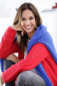 A young woman wearing a red knitted jumper with a blue jumper over her shoulders