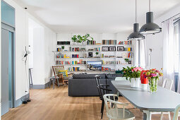 Dining table in front sofa, rocking chair and bookcase in seating area in open-plan interior