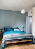 Bett mit blau-grauer Bettwäsche in Schlafzimmer mit blau gestrichenen Wänden