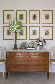 Table lamp on antique chest of drawers below etchings