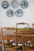 Rustic wooden table and chairs in front of decorative wall plates on white wall