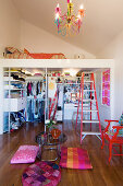 Colourful floor cushions around side table and walk-in wardrobe below loft bed in apartment