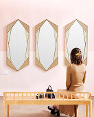 Frau sitzt auf Bank vor drei Spiegeln an rosa Wand
