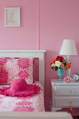 White wooden bed and white bedside cabinets in feminine, pink bedroom
