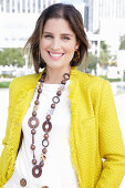 Junge Frau mit Halskette in weißem Pulli und gelber Bouclé-Jacke
