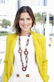 A young woman wearing a chunky necklace, a white jumper and a yellow bouclé jacket