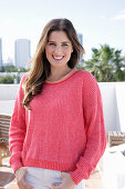 A young woman wearing a fuchsia jumper and white jeans