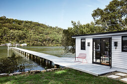 Kleines Haus mit weißer Bretterfassade am Steg auf einen See
