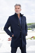 A grey-haired man on a terrace wearing a blue jacket and jeans