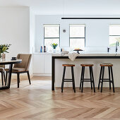 Barstools at counter and dining table in open-plan kitchen with parquet floor